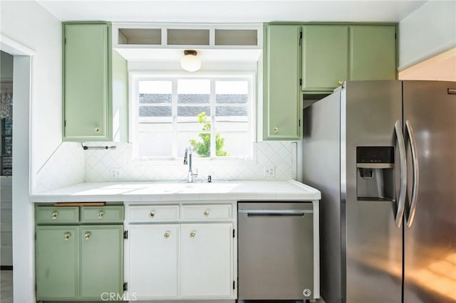 kitchen with tasteful backsplash, green cabinets, tile countertops, stainless steel appliances, and a sink