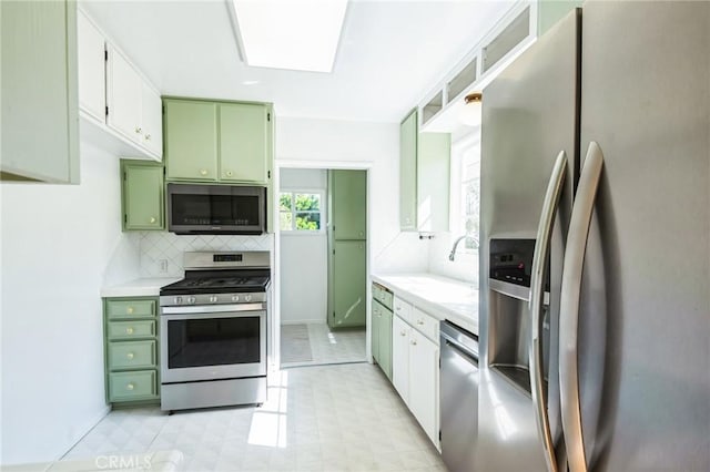 kitchen with light countertops, backsplash, green cabinetry, and stainless steel appliances