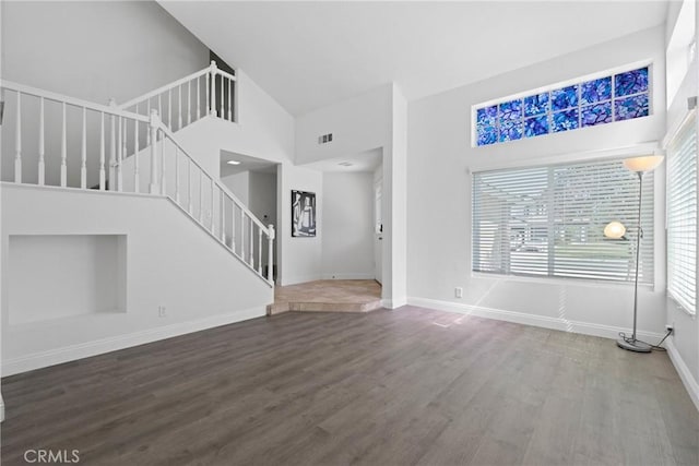 unfurnished living room with visible vents, baseboards, stairs, a high ceiling, and wood finished floors