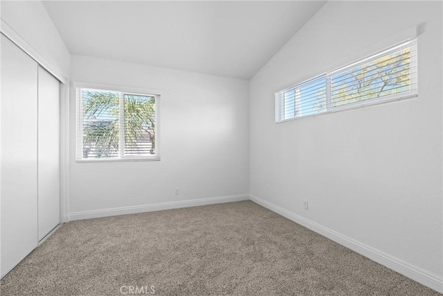 carpeted spare room featuring plenty of natural light, baseboards, and lofted ceiling