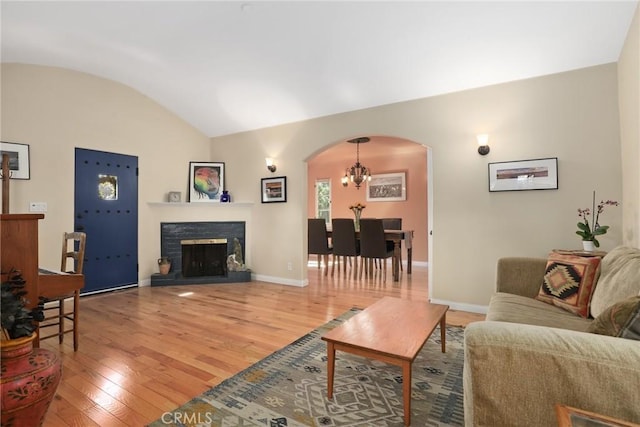 living area featuring baseboards, light wood finished floors, lofted ceiling, a fireplace with raised hearth, and arched walkways