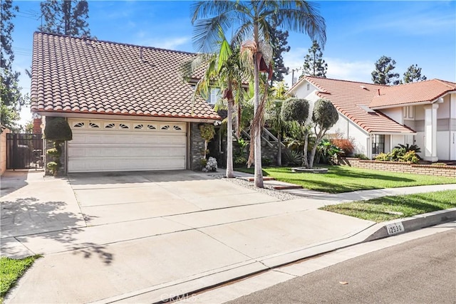 mediterranean / spanish-style house with an attached garage, concrete driveway, a tile roof, and a front yard