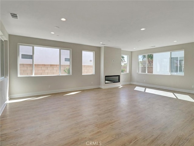 unfurnished living room with light wood finished floors, visible vents, baseboards, recessed lighting, and a glass covered fireplace