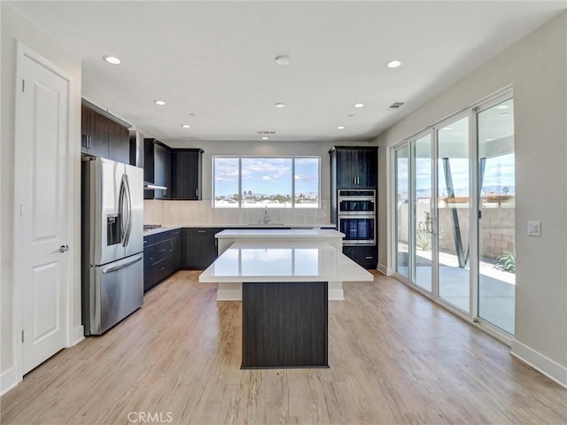 kitchen featuring light wood-style flooring, appliances with stainless steel finishes, a center island, and light countertops