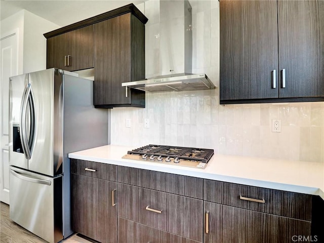 kitchen with stainless steel appliances, wall chimney exhaust hood, light countertops, decorative backsplash, and dark brown cabinets