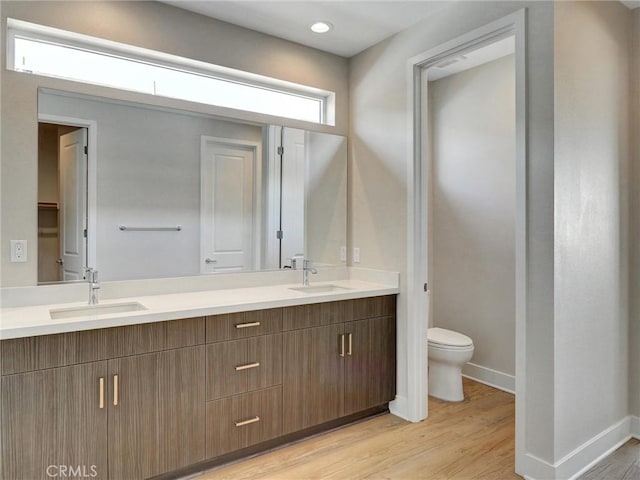 full bathroom with a sink, toilet, wood finished floors, and double vanity