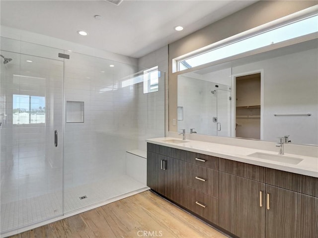 full bathroom with double vanity, wood finished floors, a stall shower, and a sink