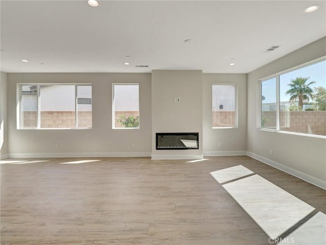 unfurnished living room featuring light wood-style floors, visible vents, and a wealth of natural light