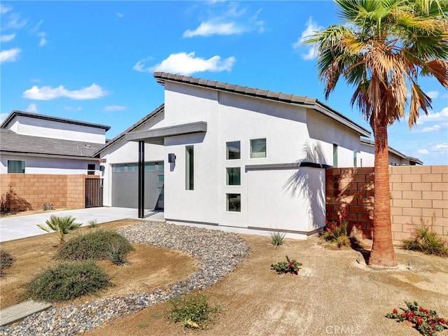 rear view of house with stucco siding, a garage, concrete driveway, and fence