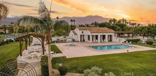 pool at dusk featuring a patio, a hot tub, a community pool, a lawn, and a mountain view