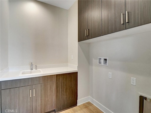 laundry room featuring baseboards, light wood finished floors, cabinet space, a sink, and washer hookup