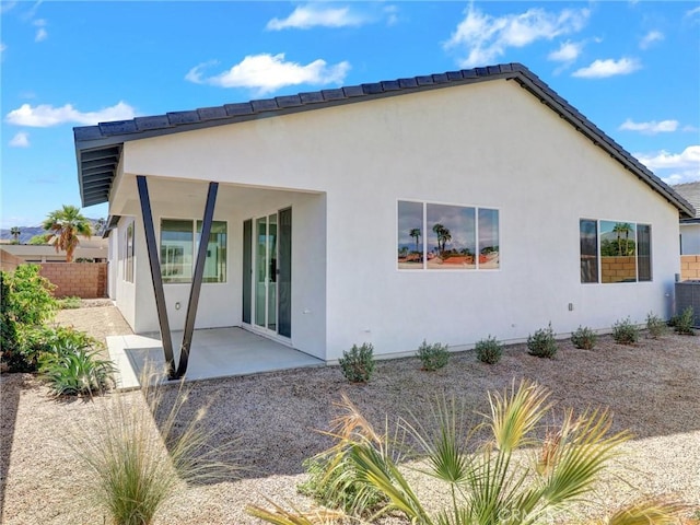 rear view of house with stucco siding, a patio, and fence