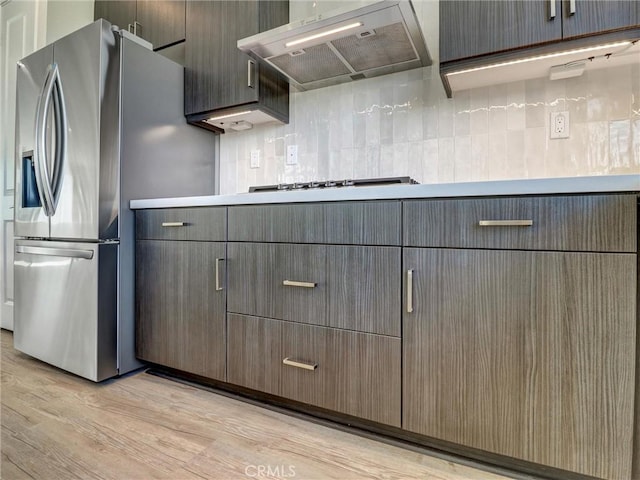 kitchen featuring light wood finished floors, premium range hood, light countertops, decorative backsplash, and stainless steel appliances