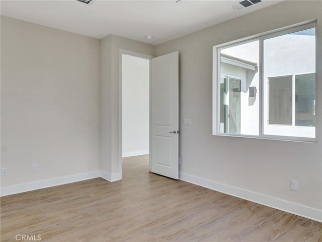 spare room with light wood finished floors, visible vents, a healthy amount of sunlight, and baseboards