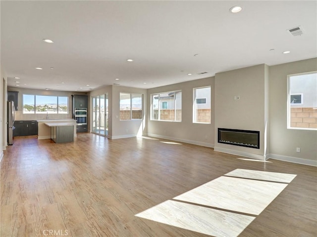 unfurnished living room featuring a glass covered fireplace, recessed lighting, light wood-type flooring, and baseboards