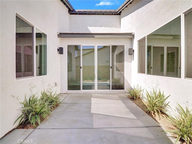 property entrance with stucco siding, a tiled roof, and a patio