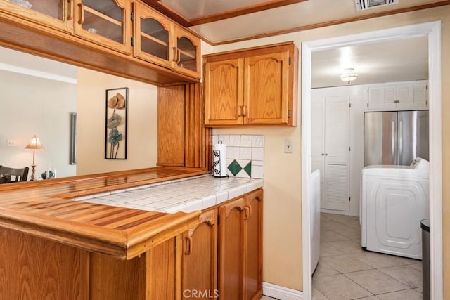 kitchen featuring washer / dryer, freestanding refrigerator, decorative backsplash, glass insert cabinets, and brown cabinets