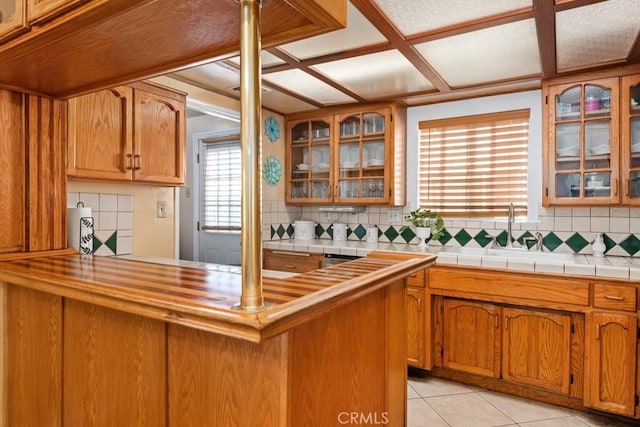 kitchen featuring tasteful backsplash, light tile patterned floors, brown cabinets, and glass insert cabinets