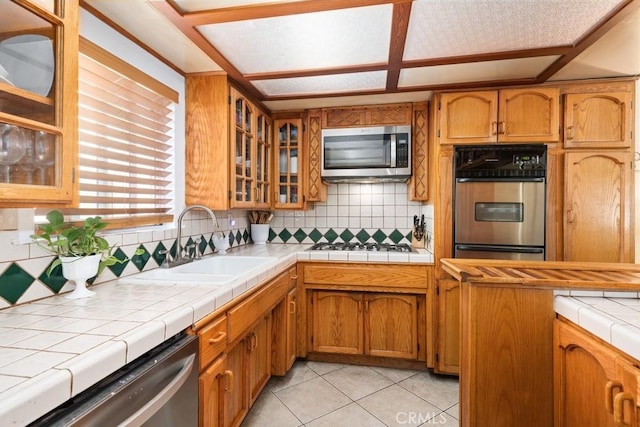 kitchen with brown cabinets, a sink, backsplash, appliances with stainless steel finishes, and light tile patterned flooring