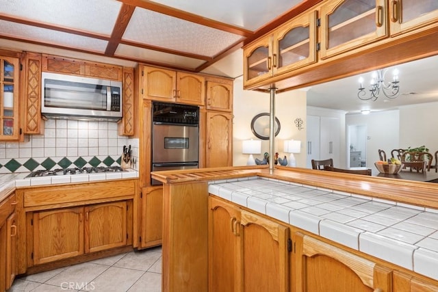 kitchen featuring light tile patterned floors, backsplash, appliances with stainless steel finishes, and brown cabinetry