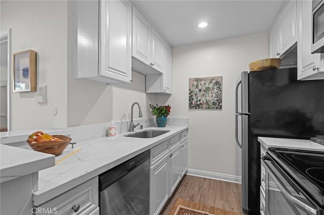 kitchen with a sink, light stone counters, wood finished floors, appliances with stainless steel finishes, and white cabinets