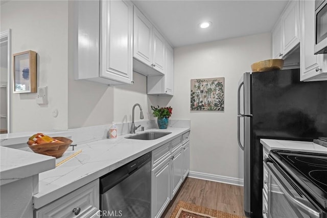 kitchen with stainless steel appliances, wood finished floors, a sink, light stone countertops, and white cabinetry