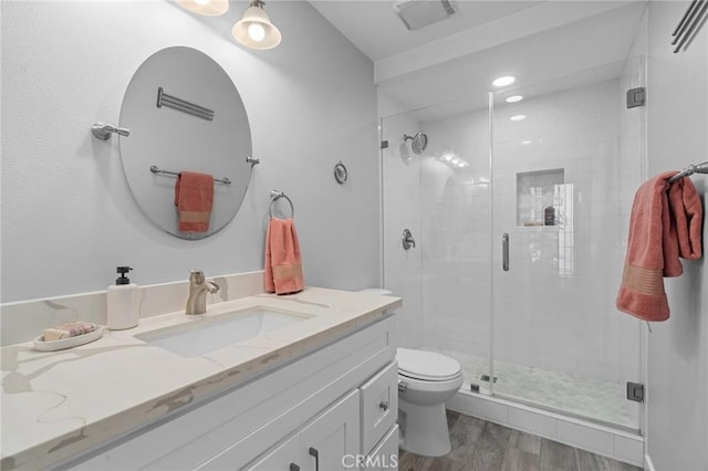 full bathroom with visible vents, toilet, wood finished floors, a shower stall, and vanity