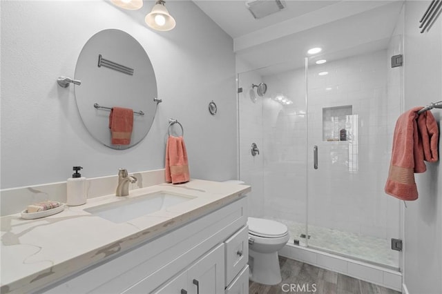 bathroom featuring toilet, visible vents, wood finished floors, a shower stall, and vanity