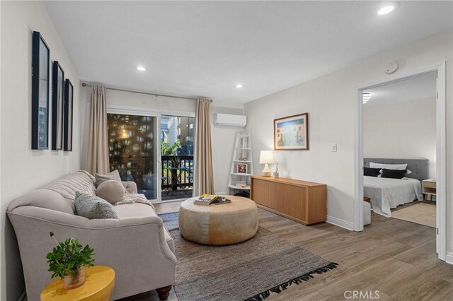 living area featuring recessed lighting, light wood-type flooring, baseboards, and a wall mounted AC