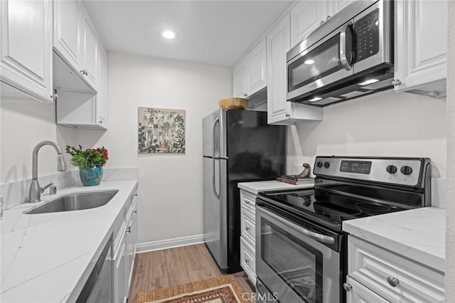 kitchen featuring white cabinets, stainless steel appliances, a sink, light wood-style floors, and light stone counters