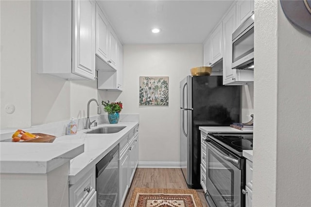 kitchen featuring baseboards, light wood-style flooring, appliances with stainless steel finishes, white cabinetry, and a sink