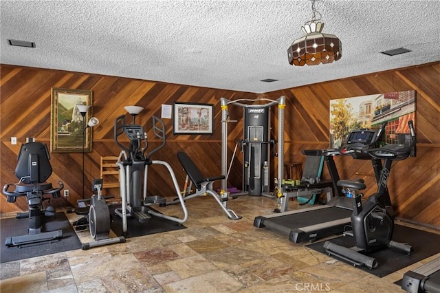 exercise room featuring wood walls and a textured ceiling