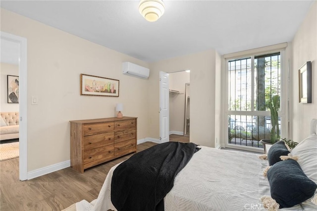bedroom featuring a walk in closet, baseboards, wood finished floors, and a wall unit AC