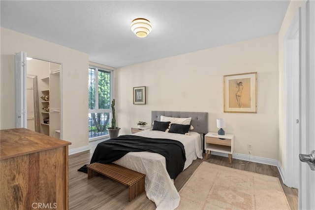bedroom featuring baseboards, wood finished floors, and a walk in closet