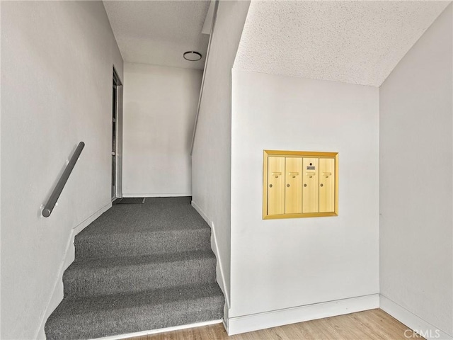 stairway featuring mail area, baseboards, a textured ceiling, and wood finished floors