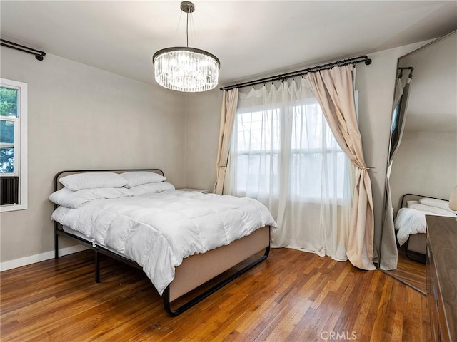 bedroom featuring an inviting chandelier, multiple windows, baseboards, and wood-type flooring