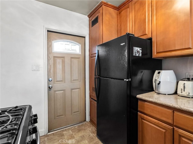 kitchen with brown cabinetry, stainless steel range with gas stovetop, and freestanding refrigerator