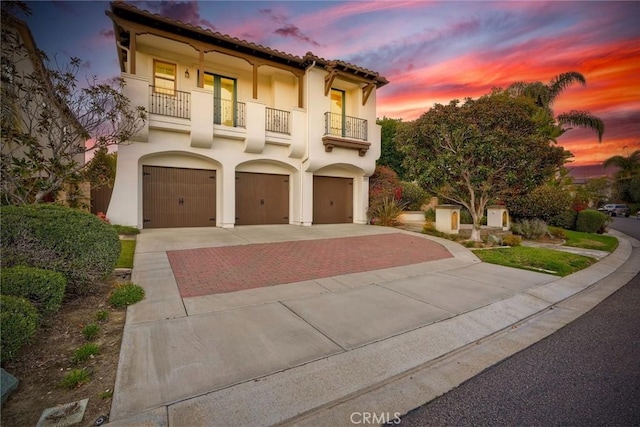 mediterranean / spanish-style house with a tiled roof, a balcony, decorative driveway, and stucco siding