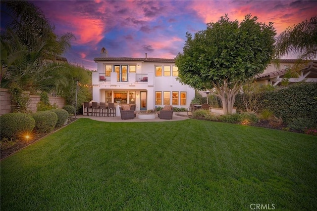 back of house at dusk featuring a patio, a balcony, an outdoor living space, stucco siding, and a lawn