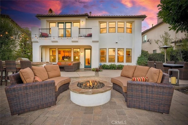 rear view of property with an outdoor living space with a fire pit, a balcony, a patio area, and stucco siding