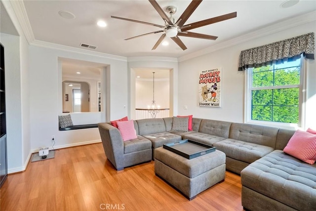 living area with visible vents, crown molding, baseboards, light wood-style flooring, and ceiling fan with notable chandelier