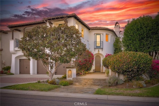 mediterranean / spanish house with stucco siding, a tile roof, decorative driveway, a garage, and a balcony