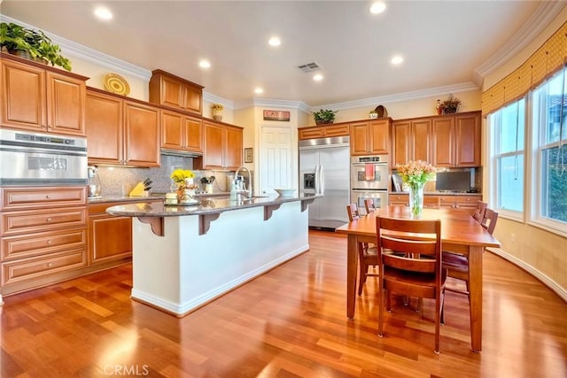 kitchen with a breakfast bar area, brown cabinetry, visible vents, and stainless steel appliances