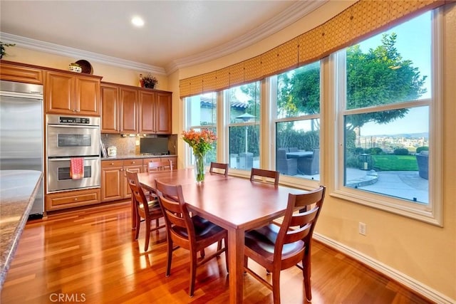 dining space with light wood finished floors, crown molding, and baseboards