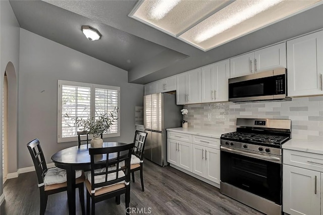 kitchen featuring dark wood-type flooring, arched walkways, appliances with stainless steel finishes, white cabinets, and vaulted ceiling