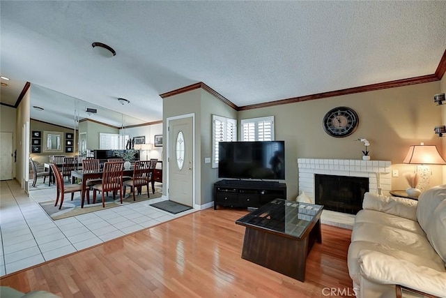 living room featuring light wood-type flooring, a textured ceiling, crown molding, lofted ceiling, and a brick fireplace