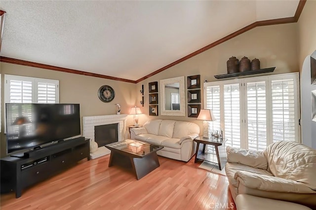 living room with ornamental molding, a textured ceiling, wood finished floors, a brick fireplace, and vaulted ceiling