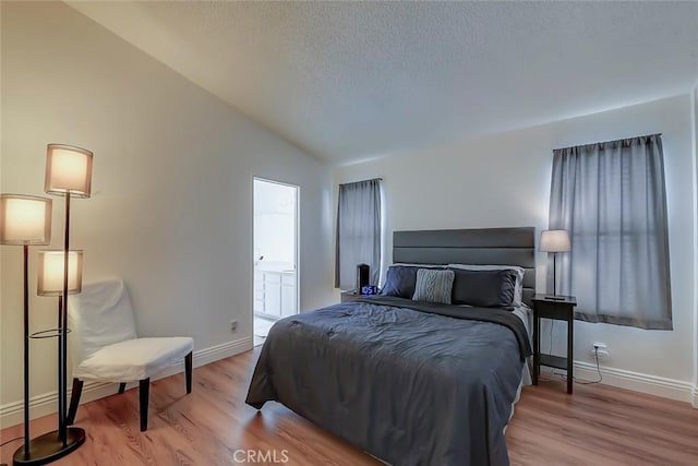 bedroom with lofted ceiling, wood finished floors, baseboards, and a textured ceiling