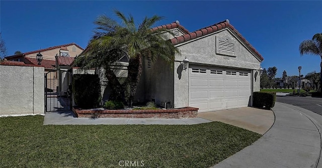 view of side of home featuring stucco siding, a lawn, driveway, a gate, and a tiled roof