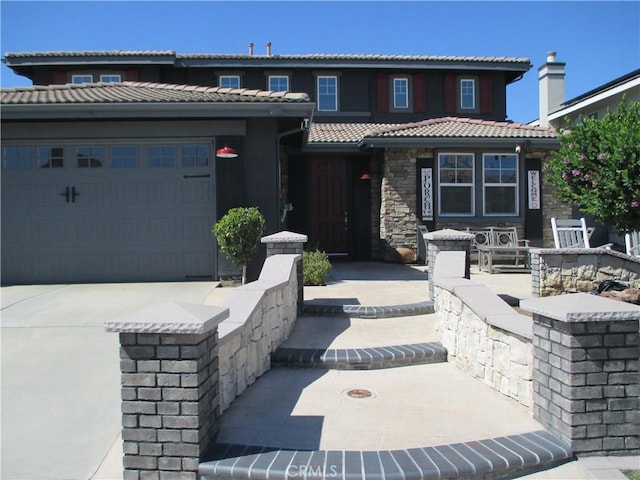 view of front of property featuring a tiled roof, an attached garage, stone siding, and driveway